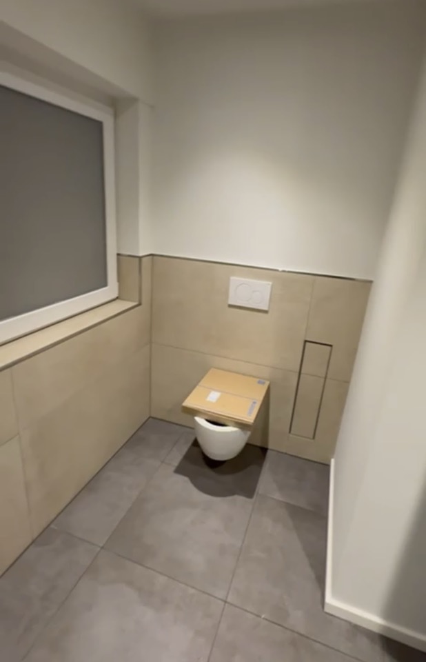 Wandhängendes WC mit großformatigen Wandfliesen und modernem Spülmodul